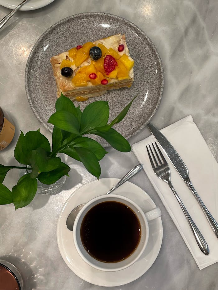 Tasty fruit-topped dessert and coffee on a marble table, perfect for a cozy cafe vibe.