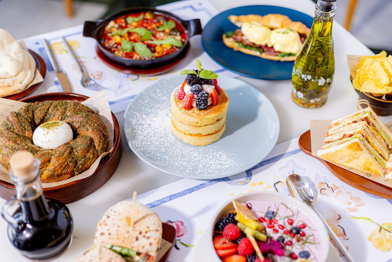 A colorful brunch spread featuring pancakes, fresh fruits, pastries, and sandwiches.